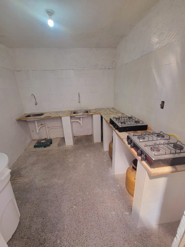 Cocina con mesada de piedra en L, dos piletas de acero inoxidable y canillas de pared, con dos anafes apoyados encima.
