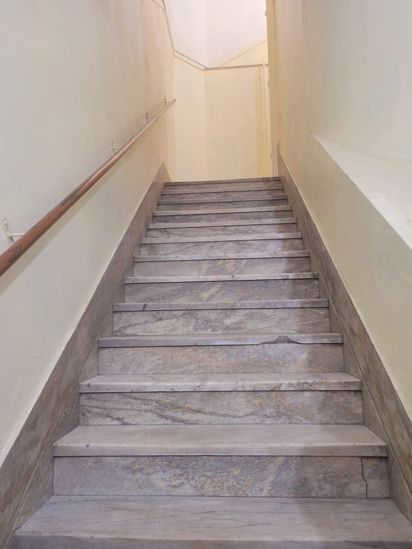 Escalera de mármol de un edificio, con el pasamanos de bronce recolocado y las paredes recién pintadas.