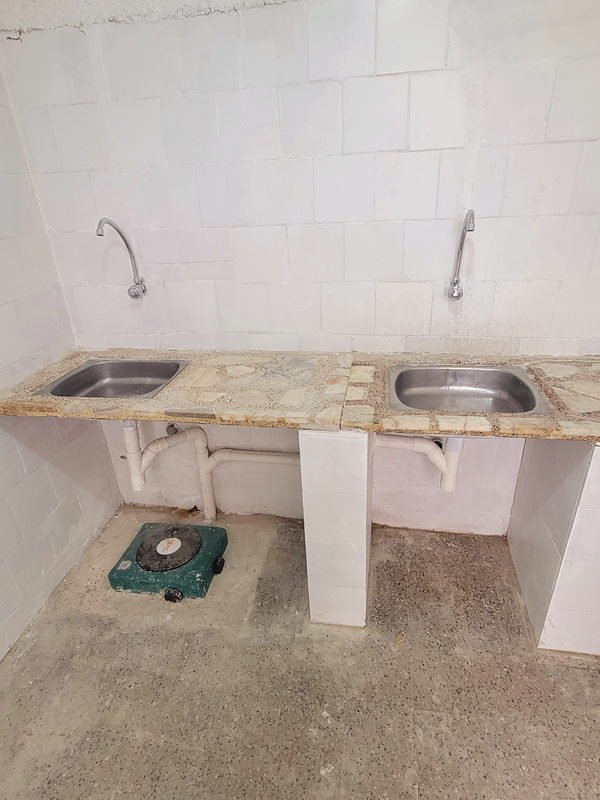 Mesada de piedra con dos piletas y canillas cromadas ya instaladas, con los desagües de PVC a la vista debajo.