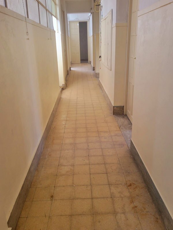 Pasillo largo de un edificio antiguo ya pintado, con el piso de baldosa original y la instalación eléctrica todavía a la vista sobre la pared.